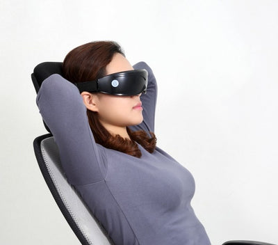 White and black eye massager with a goggle-like design, featuring a white frame and dark lenses, on a wooden surface. - Image 6