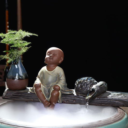 Ceramic flowing water ornament with a meditating monk figurine, small plant, and misting humidifier in a teal and brown bowl. - Image 5
