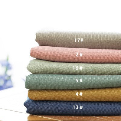 Stack of six folded fabric swatches in beige, pink, sage green, teal, mustard yellow, and navy blue.
