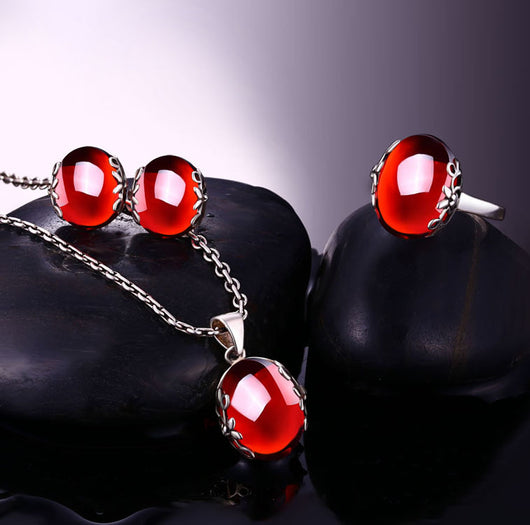 Silver ring with a large, round, deep red gemstone set in an ornate filigree bezel, displayed on a textured surface.
