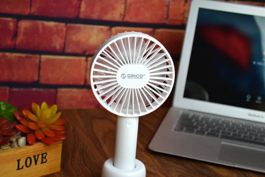 White ORICO FH1 handheld USB fan with charging dock, USB cable, and user manuals on a wooden desk. - Image 5