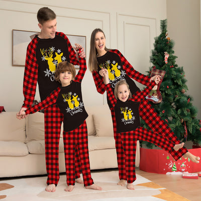 Two children in matching black and red buffalo plaid Christmas pajamas with golden deer and "Merry Christmas" print.