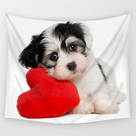 Cute black and white Shih Tzu puppy resting its head on a red heart pillow on a white tapestry.