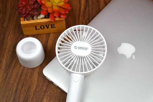 White ORICO FH1 handheld USB fan with charging dock, USB cable, and user manuals on a wooden desk. - Image 3