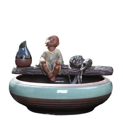 Ceramic flowing water ornament with a meditating monk figurine, small plant, and misting humidifier in a teal and brown bowl. - Image 14
