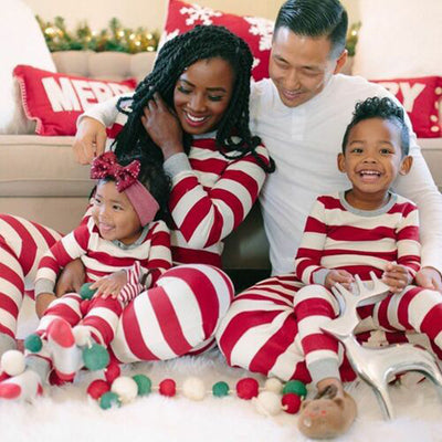 Family of four in matching red and white striped Christmas pajamas, sitting on a white rug with holiday decor. - Image 9