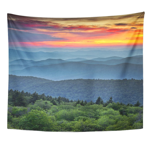 Printed tapestry featuring a vibrant sunset over layered blue mountains and a lush green forest.