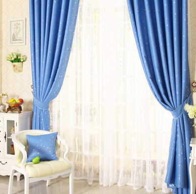 Blue star print curtains tied back to reveal sheer white curtains, in a bright room with a white chair.