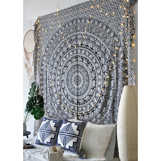 Black and white mandala tapestry with string lights hanging above a bed with blue and white patterned pillows. - Image 12