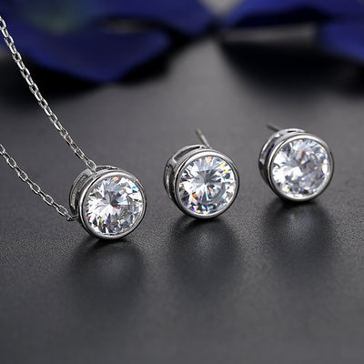 Silver-tone necklace and stud earrings set with round, bezel-set clear gemstones, ideal for bridal or formal wear.