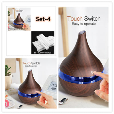 Dark wood grain LED essential oil diffuser with a blue light band and touch switch, shown with a hand operating it. Includes a bundle of 10 white filter sticks. - Image 13