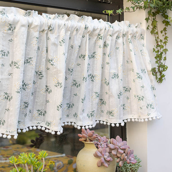 White semi-sheer curtain with green and grey floral pattern and cream tassel trim, hanging in a window.