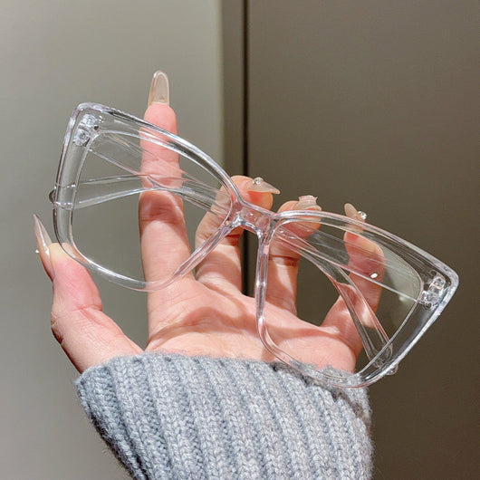 Clear large-frame square glasses held by a hand in a grey knitted sweater, showcasing the transparent plastic frame. - Image 15