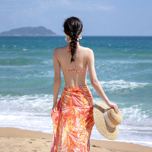 Woman in an orange and pink patterned halter neck backless cover-up dress with a straw hat on a sandy beach. - Image 7