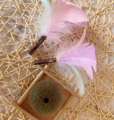 Green catnip ball toy with pink, purple, and white feathers attached, designed for cats to play and nibble. - Image 9