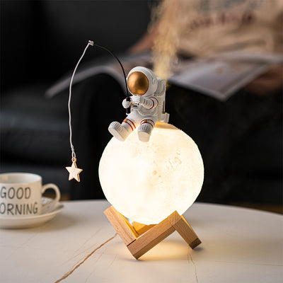 Astronaut figurine sitting on a glowing moon lamp, holding a fishing rod with a star charm, on a wooden stand.