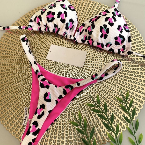 White textured bikini with red cherry print, featuring a triangle top and tie-side bottoms, on a woven mat.