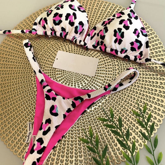 White textured bikini with red cherry print, featuring a triangle top and tie-side bottoms, on a woven mat.