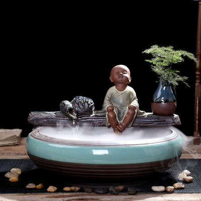 Ceramic flowing water ornament with a meditating monk figurine, small plant, and misting humidifier in a teal and brown bowl. - Image 7