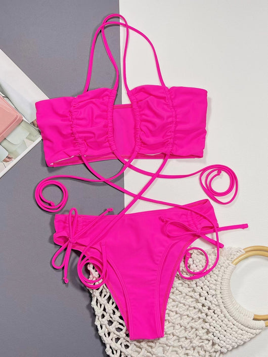 Neon pink lace-up bikini with a bandeau top and high-cut bottom, laid flat on a split gray and white background. - Image 14