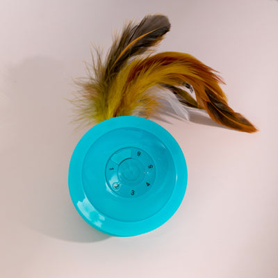 Teal cat toy with a feather and bell attachment, held in a hand against a blue and beige background. - Image 6