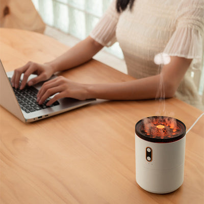 White volcanic flame aroma essential oil diffuser emitting orange light and mist on a wooden desk next to a laptop. - Image 3