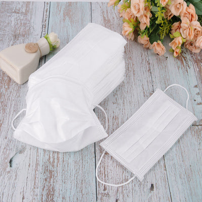 Stack of pink disposable non-woven face masks, with one unfolded and one folded, on a light wood surface. - Image 3