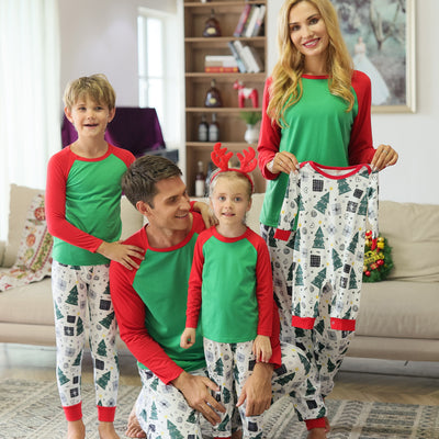 Family of four in matching red and green Christmas pajamas with tree and gift prints, mother holds baby romper. - Image 7