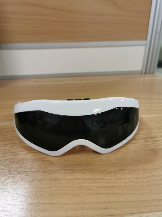 White and black eye massager with a goggle-like design, featuring a white frame and dark lenses, on a wooden surface. - Image 9
