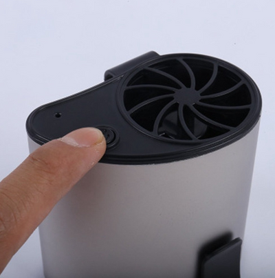 Close-up of a finger pressing the power button on a silver-grey portable waist fan with a black fan grill. - Image 7