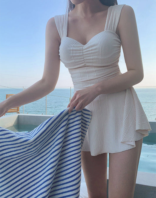 Woman in a cream ribbed one-piece swimsuit with a sweetheart neckline and skirted bottom, sitting on a lounge chair. - Image 20