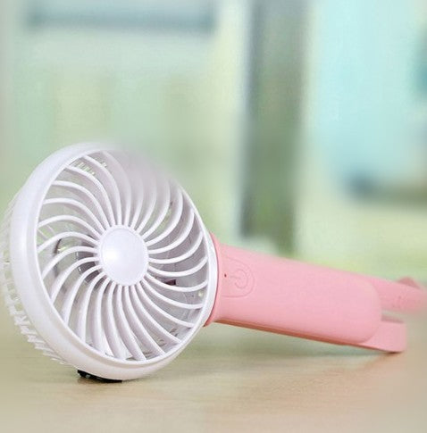 Lime green and white mini USB portable fan with a flexible strap, lying on a light wooden surface.