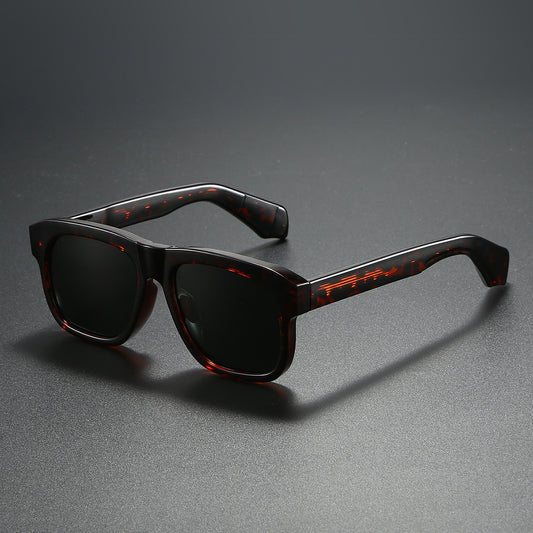 Black square-frame polarized sunglasses with dark lenses, suitable for both men and women, on a dark gray surface.