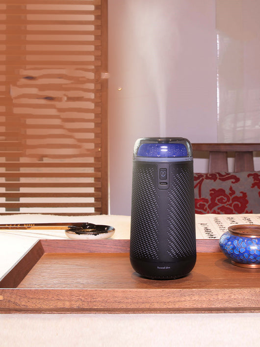 Black car aroma diffuser humidifier with blue light, wireless charging, and automatic spray, shown with six essential oil bottles.