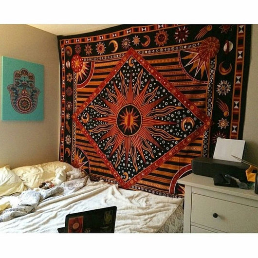 Black, orange, and red celestial tapestry with a large sun, moons, and stars, hanging above a bed.