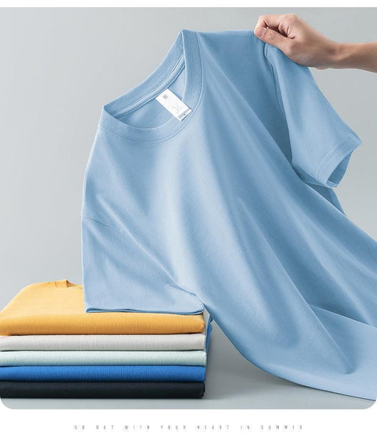 Light gray short-sleeve t-shirt with a round neck, held up to show its smooth fabric. A stack of folded t-shirts in various colors is visible in the background. - Image 15