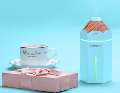 Light blue pencil-shaped mini humidifier with wood-grain top and glowing green light, next to a white teacup and pink gift box. - Image 5