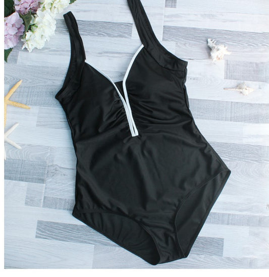 Woman in black one-piece swimsuit with white trim, wide-brimmed hat, and striped tote bag on a sunny beach. - Image 2