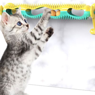 Grey tabby kitten playing with a yellow and teal wall-mounted cat toy featuring a track with rolling balls.