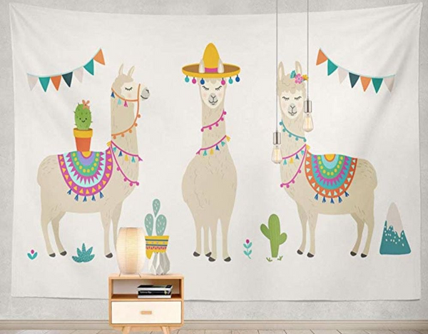 White tapestry featuring three cartoon llamas with colorful saddles, a sombrero, flowers, cacti, and mountains.