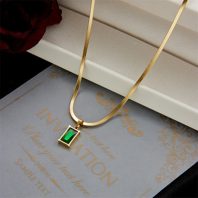 Gold hoop earrings with rectangular emerald green zircon pendants, displayed on a light beige fabric. - Image 3