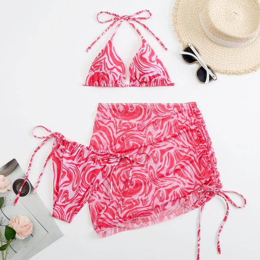 Women's three-piece swimsuit in red and orange abstract swirl print, featuring a halter bikini top, tie-side bottoms, and a ruched mini skirt. - Image 3
