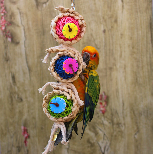 Colorful bird toy with three woven vine balls, internal pink, blue, and green string, felt flowers, and a bell.