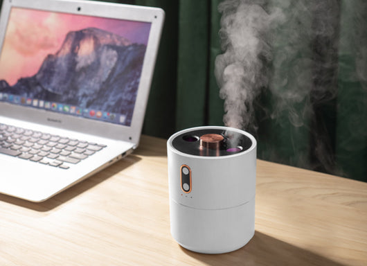 White volcanic flame aroma essential oil diffuser emitting orange light and mist on a wooden desk next to a laptop. - Image 17