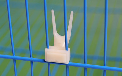 White plastic bird fruit fork clipped onto blue birdcage bars, designed to hold fruit or vegetables for pet birds. - Image 18