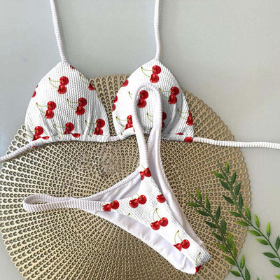White textured bikini with red cherry print, featuring a triangle top and tie-side bottoms, on a woven mat. - Image 23