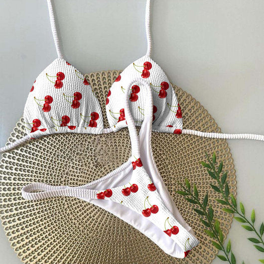 White textured bikini with red cherry print, featuring a triangle top and tie-side bottoms, on a woven mat. - Image 23