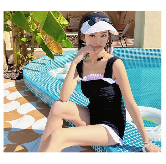 Black one-piece swimsuit with white ruffled trim and ruched bodice, modeled by a woman next to a swimming pool. - Image 13
