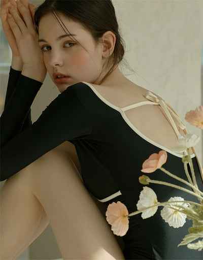 Woman wearing a black long-sleeve one-piece swimsuit with a wrap-style V-neck and light cream trim. - Image 17