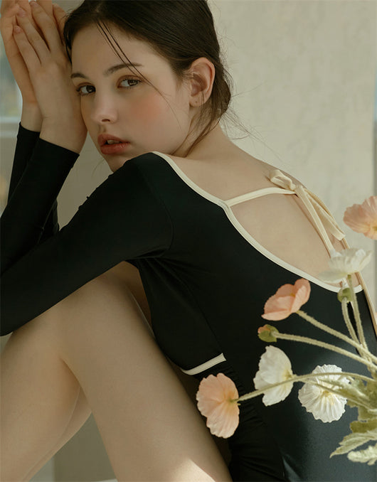 Woman wearing a black long-sleeve one-piece swimsuit with a wrap-style V-neck and light cream trim. - Image 17